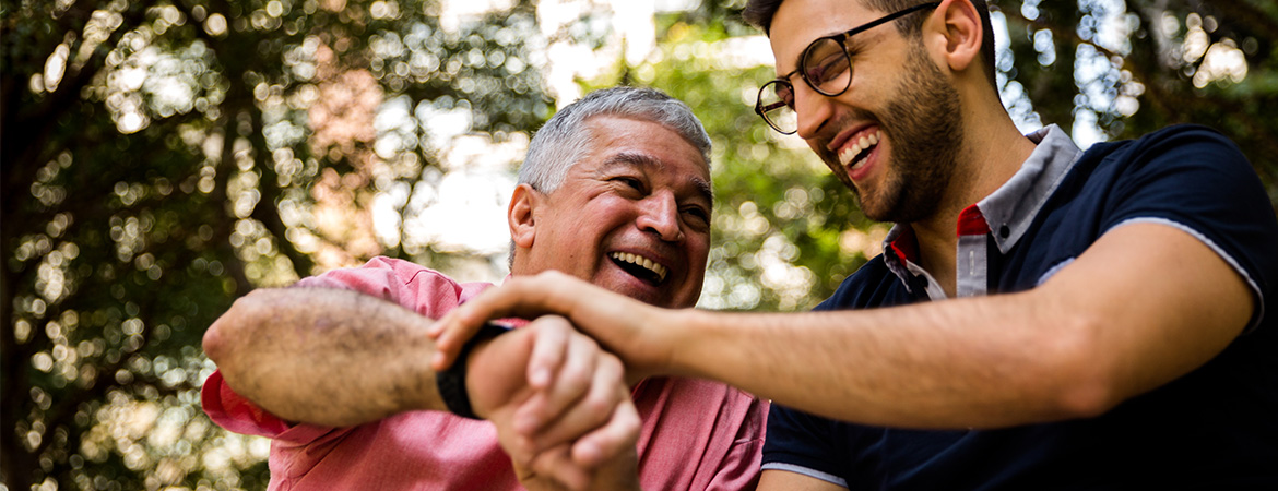 Elderly father and middle aged son smiling looking at fathers wristwatch