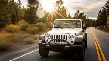 Photo of man driving jeep with female passenger on forest road