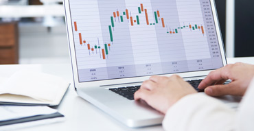 Hands typing on laptop displaying a candlestick chart