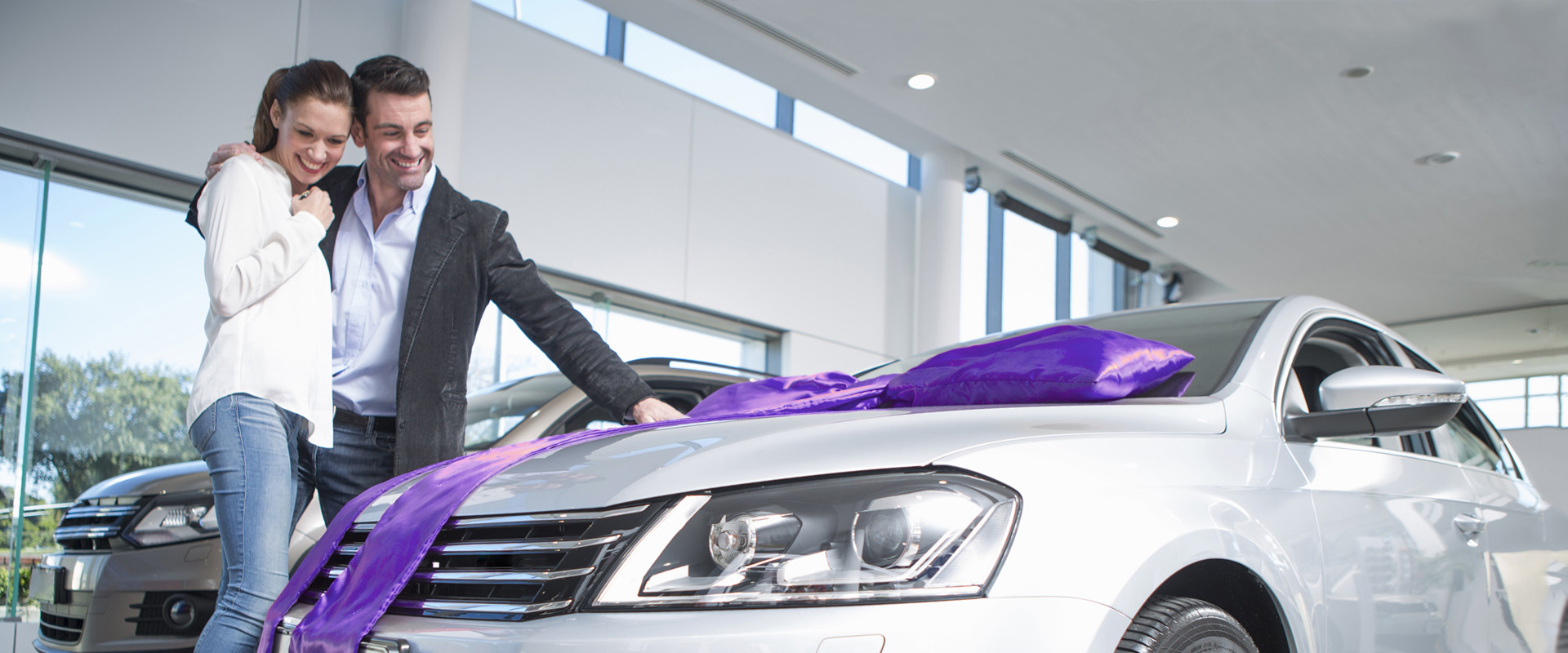 Couple standing next to new car with purple bow