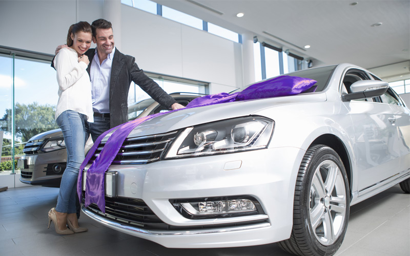 Couple standing next to new car with purple bow
