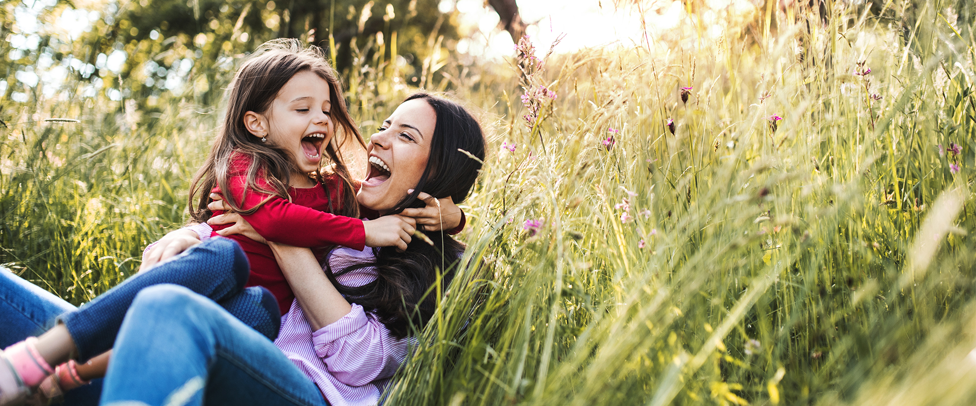 Mother and Daughter Laughing and Hugging on Grassy Hillside