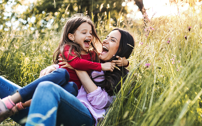 Mother and Daughter Laughing and Hugging on Grassy Hillside