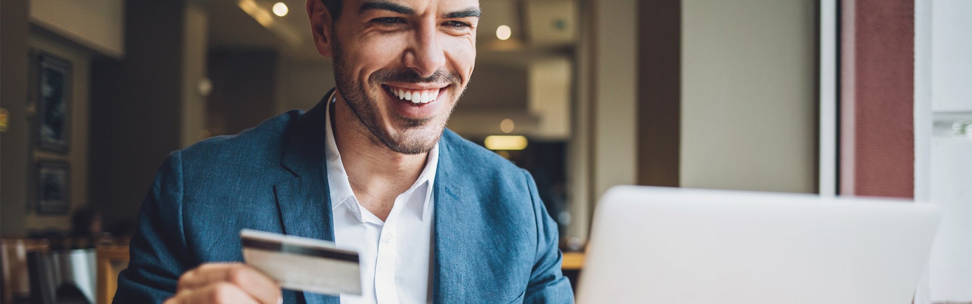 man looking at a computer screen smiling, with a card in his hand