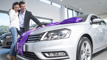 Man and woman looking at new vehicle in auto dealership with a purple bow on hood