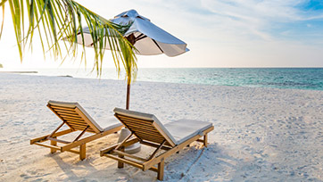 Two empty lounge chairs on the beach under an umbrella