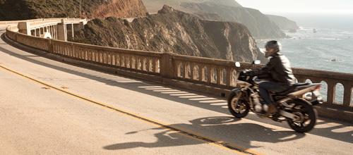 Person on motorcycle riding down scenic road along mountain by ocean