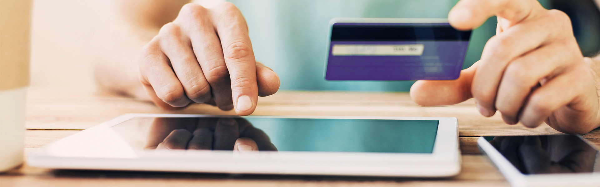 Hand holding purple credit card while typing on a tablet