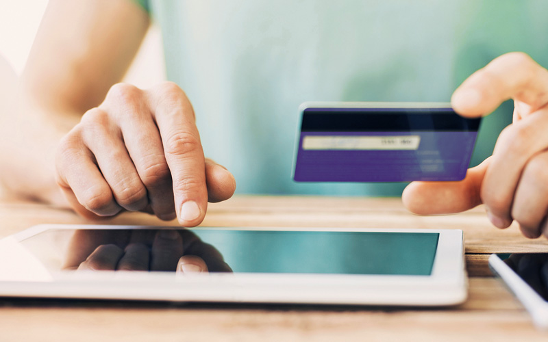 Hand holding purple credit card while typing on a tablet