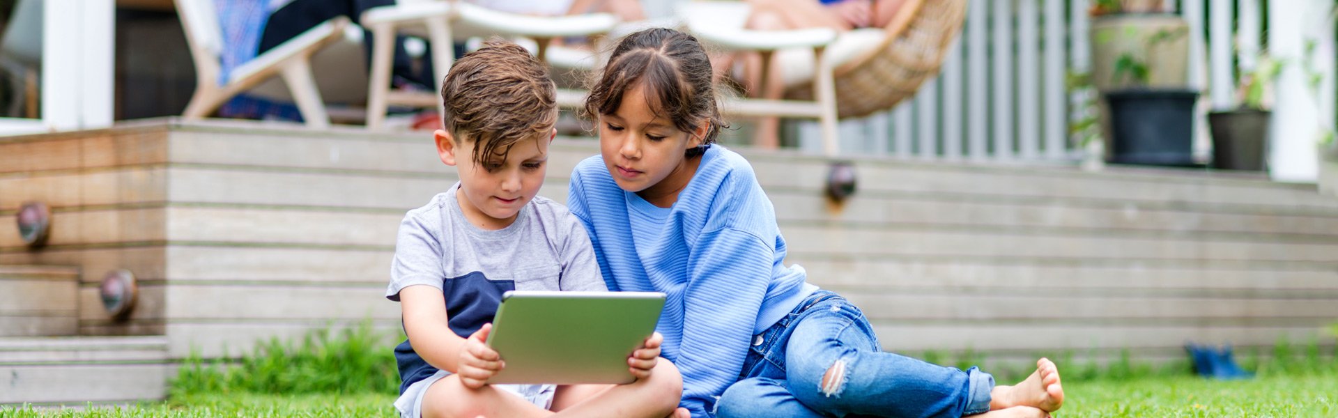 Two children viewing a tablet sitting in lawn