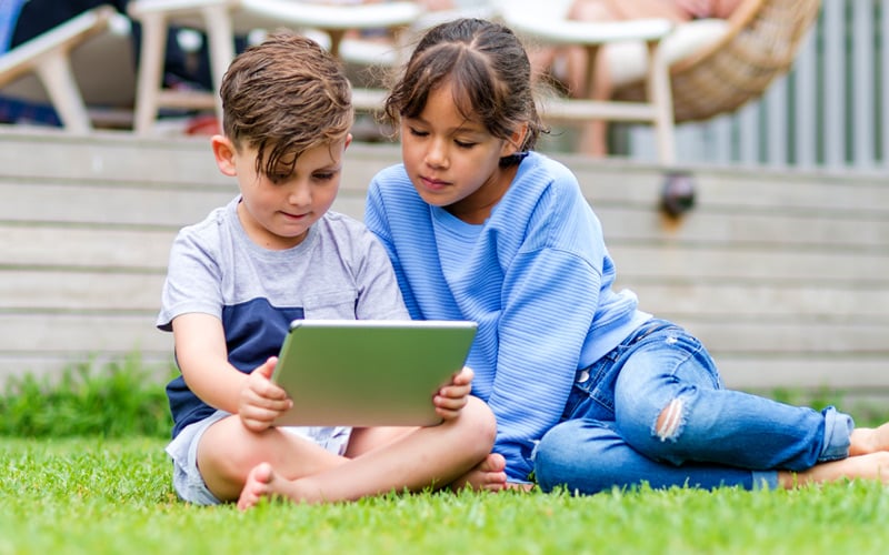 wo children viewing a tablet sitting in lawn