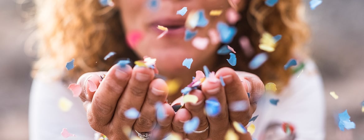 Woman blowing multicolored confetti out of the palms of her hands