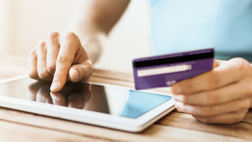 Photo of hand holding a credit card while using a tablet