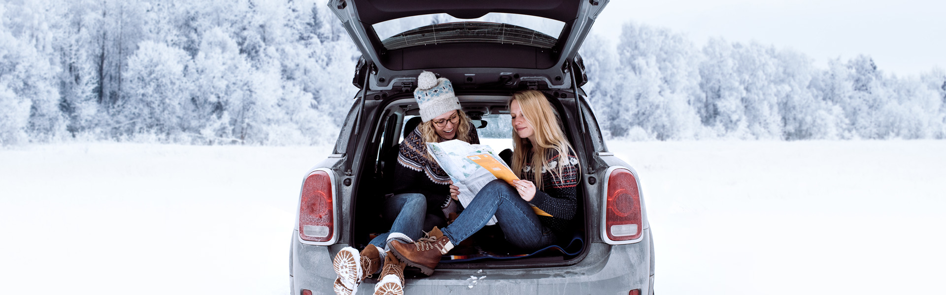 Two women sitting in the back hatch of a vehicle while it snows