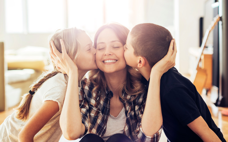 Two young children kissing their mother