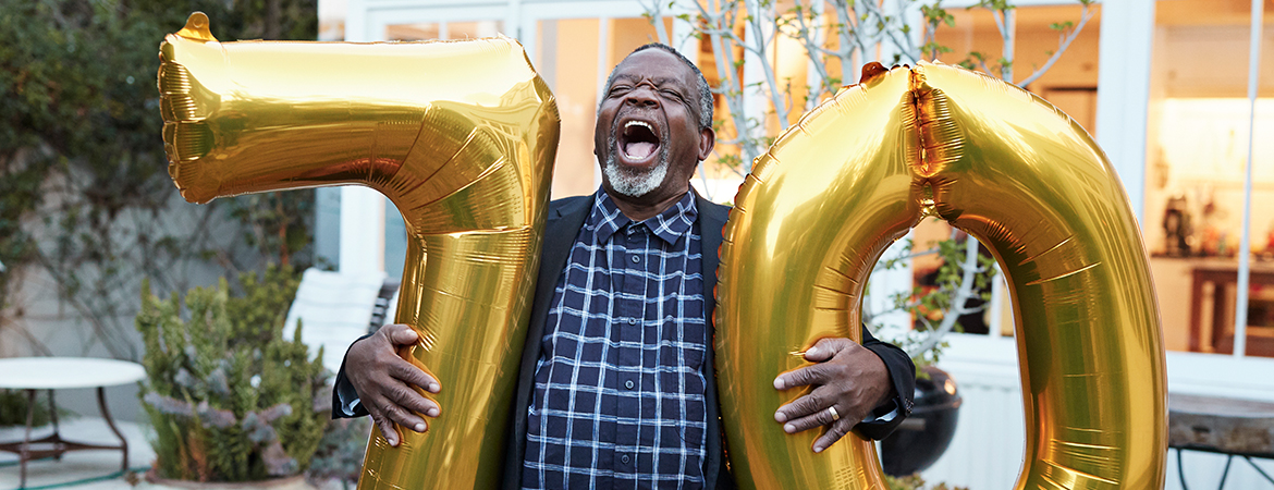 Man holding up balloons shaped like the numbers 7 and 0 to celebrate birthday