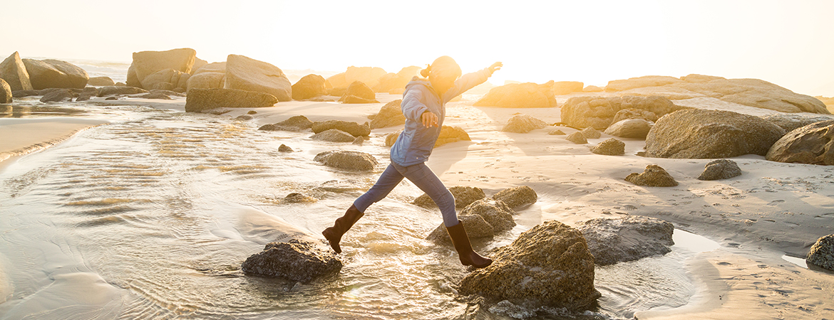 Woman jumping across rocks on beach coast