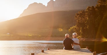 Elderly couple sitting on lake pier looking at view