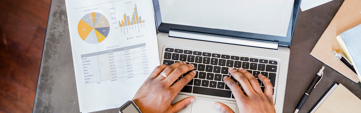 Person using laptop with document showing a financial statement next to them