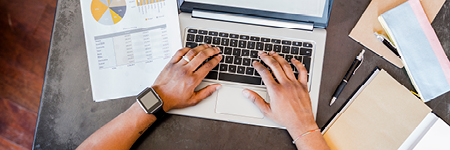 Person using laptop with document showing a financial statement next to them