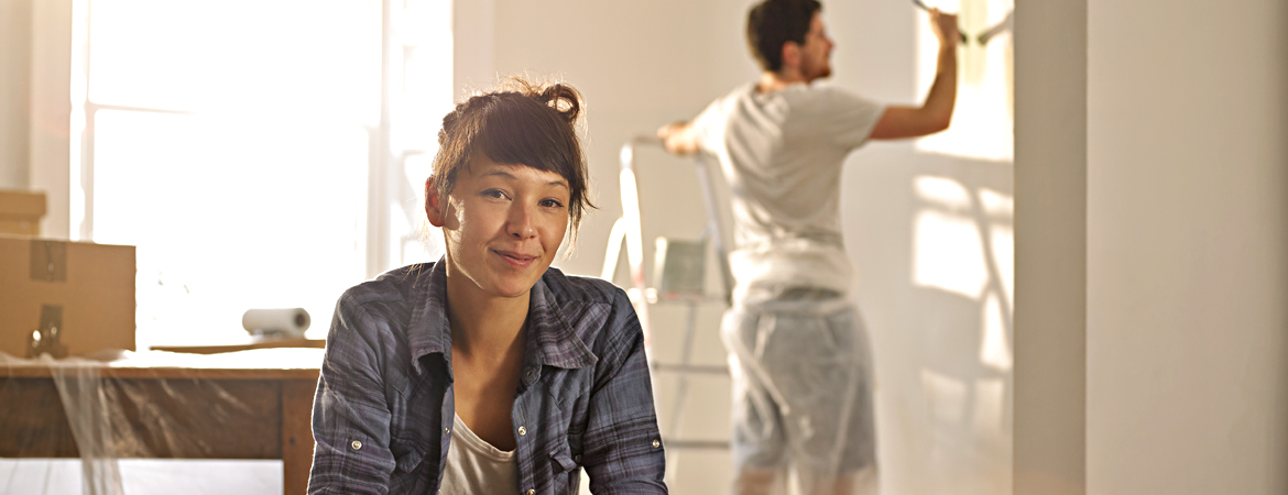 New homeowner taking a break while partner continues painting wall in background