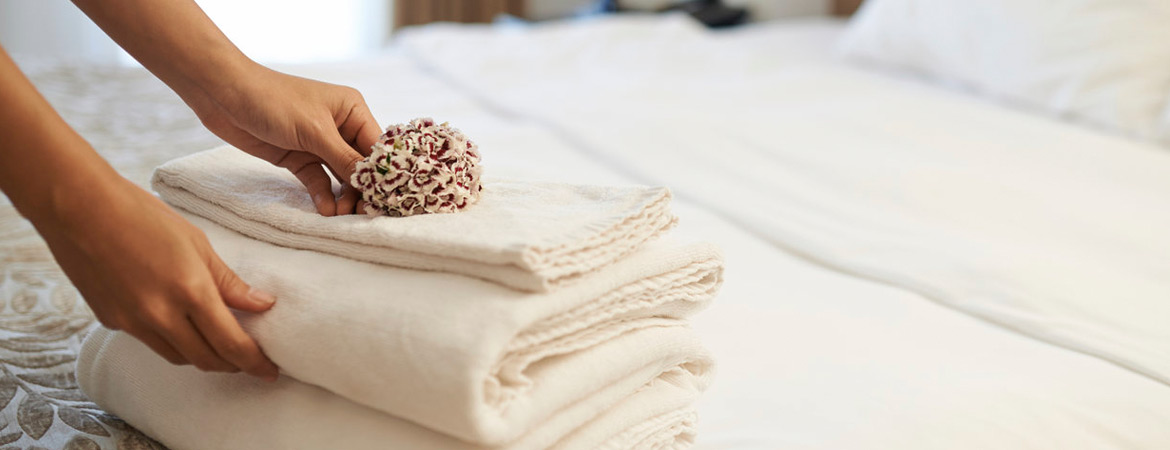 Woman staging a home by placing flowers on stack of clean white towels folded on a neatly made bed